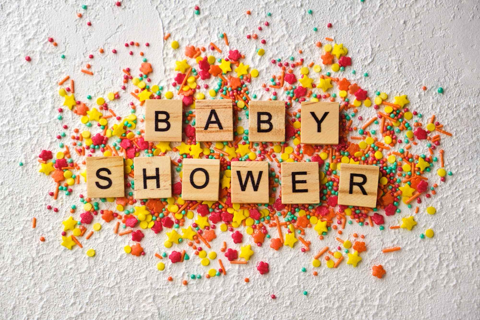 baby shower written in wooden words with colorful confetti white textured background