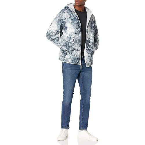 A man wearing blue jeans and white shoes keeps his hands inside the gray and white puffer jackets pocket A man wearing blue jeans and white shoes keeps his hands inside the gray and white puffer jackets pocket