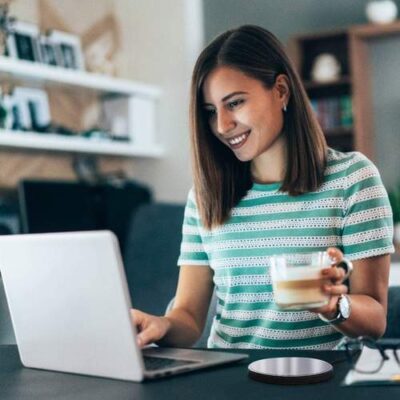 A student working in the computer and drinks coffee and kept the coffee warmer to have her coffee warm until she completes to drink