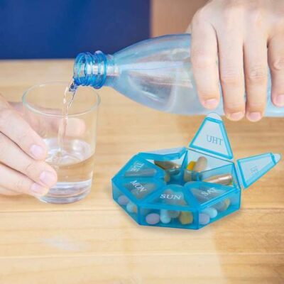 Tablets are organized in weekly pill organizer and a hand pouring water in the glass