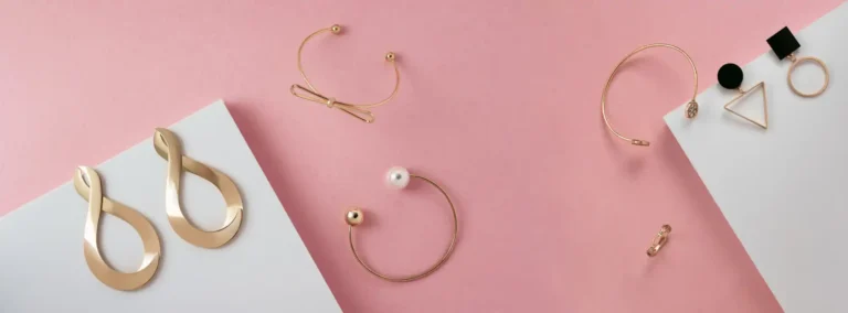 panoramic top view modern golden jewelry accessories with pink white surface