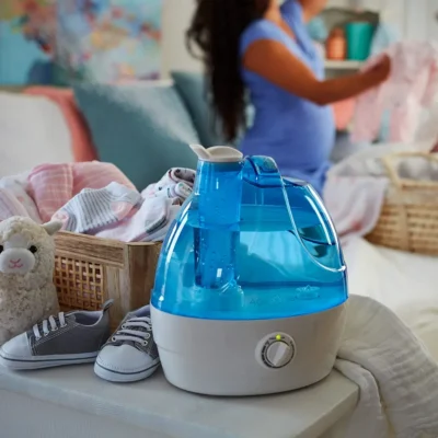 A pregnant woman folding her clothes kept the chill humidifier in her room on the table along with socks plush toy and baby socks