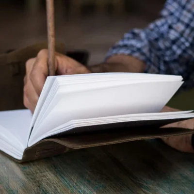 A man wearing watch writing in a leather journal